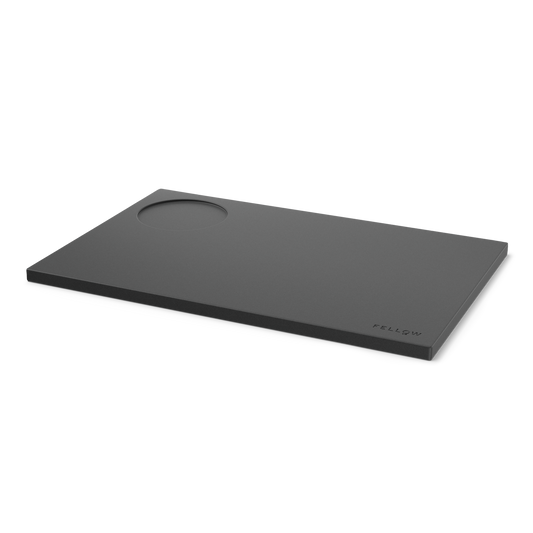 Fellow Espresso Tamping Mat: rectangular black silicone with a circular indent and logo.